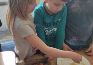Dzieci przygotowują składniki na pizzę.